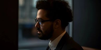 Profile of a man in glasses and suit in dim light.