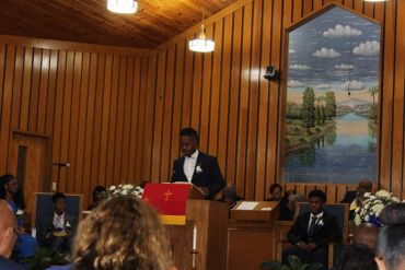 Man speaking at a wooden church pulpit during a service.