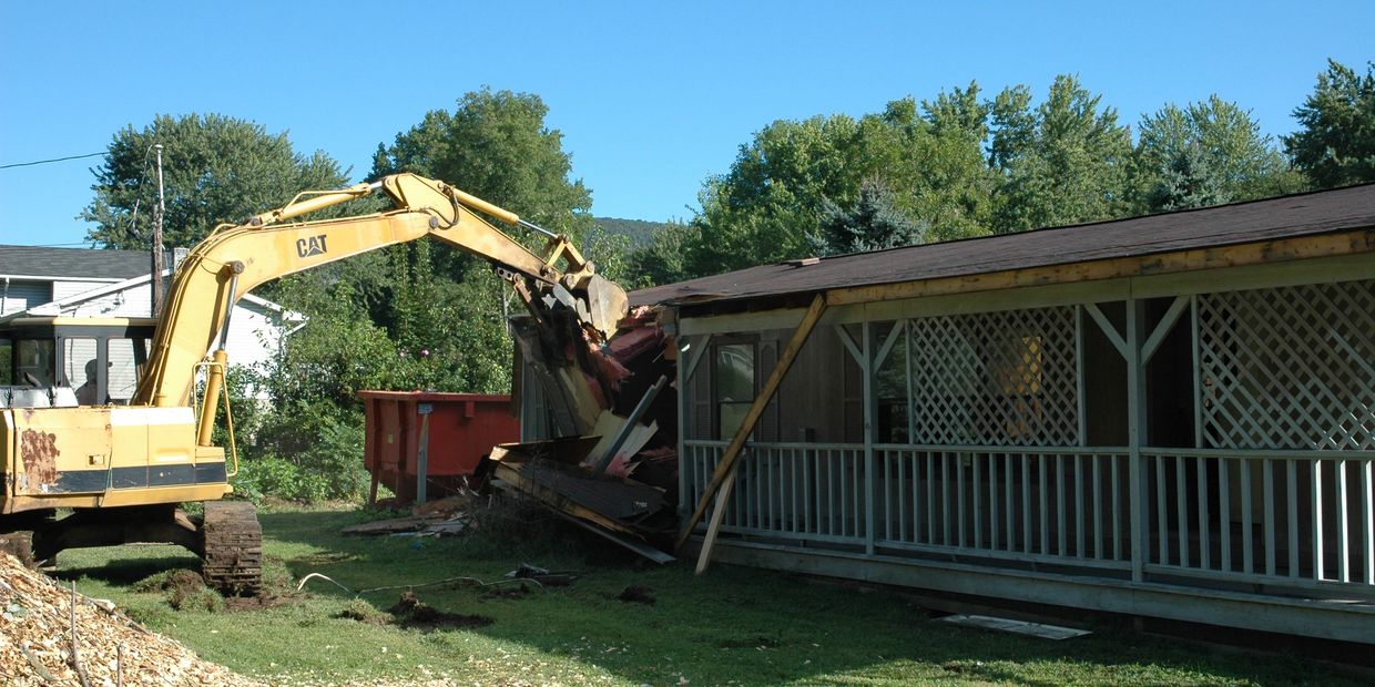 A yellow excavator demolishing a house on a sunny day.
