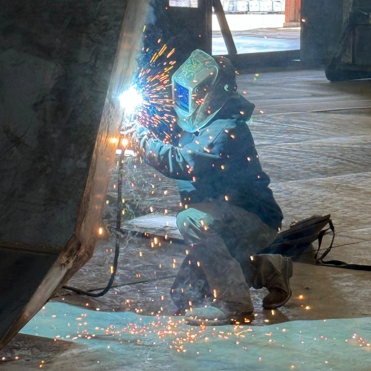 Metal fabrication welder assembling roll-off dumpster with welding torch.