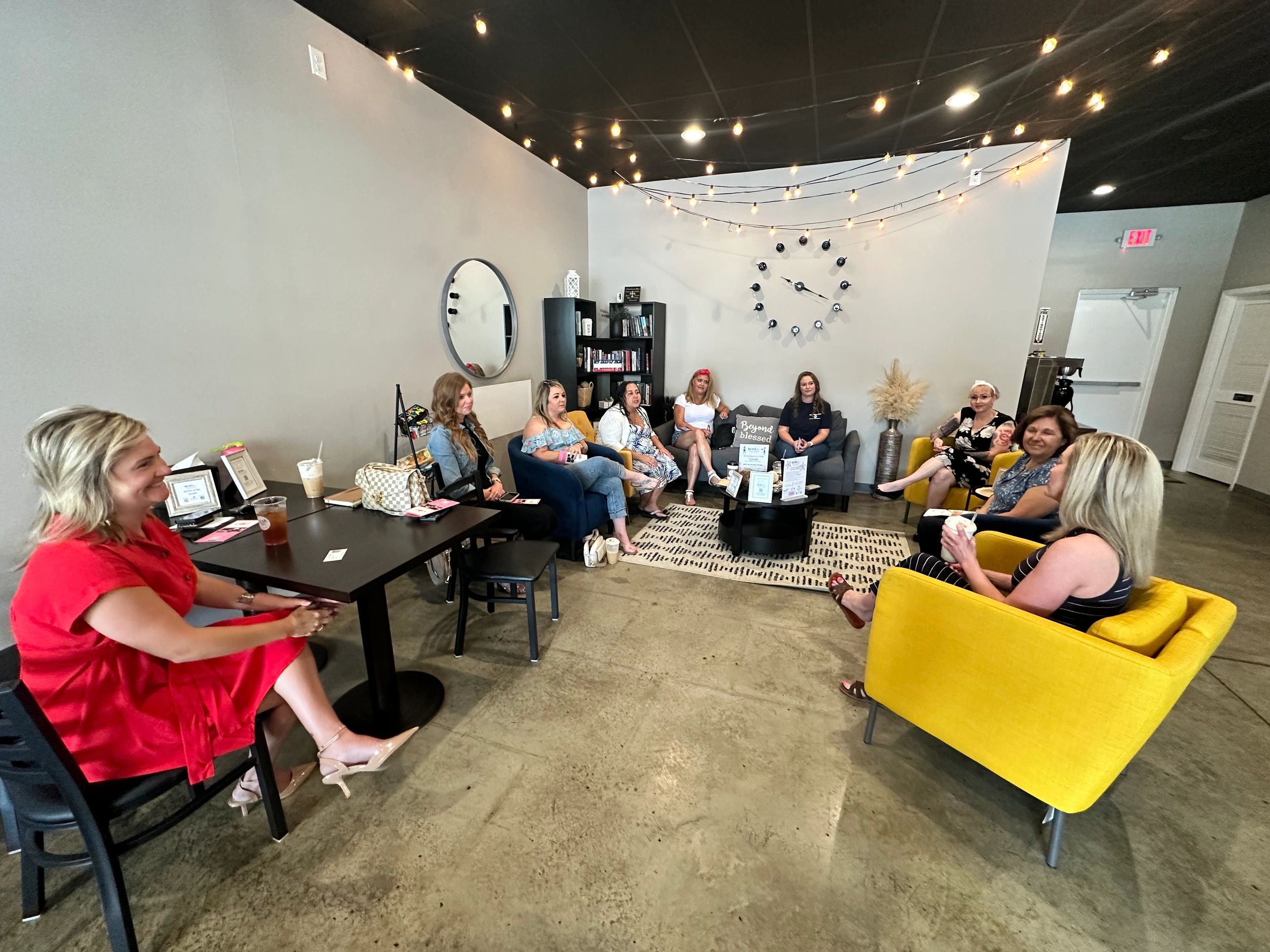 Women gathered in a cozy, modern living room with string lights and yellow chairs.