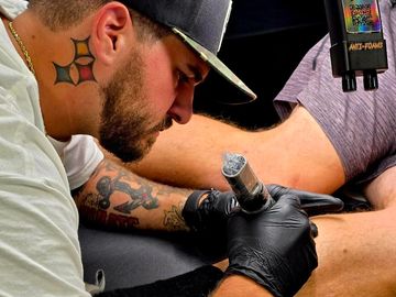 Tattoo artist focused on inking a client's leg.