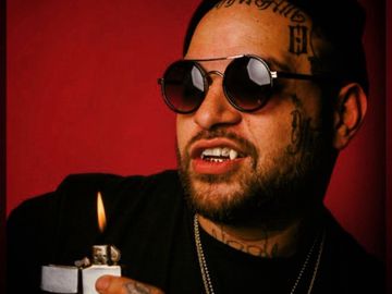 Man with tattoos and sunglasses lighting a lighter against a red background.