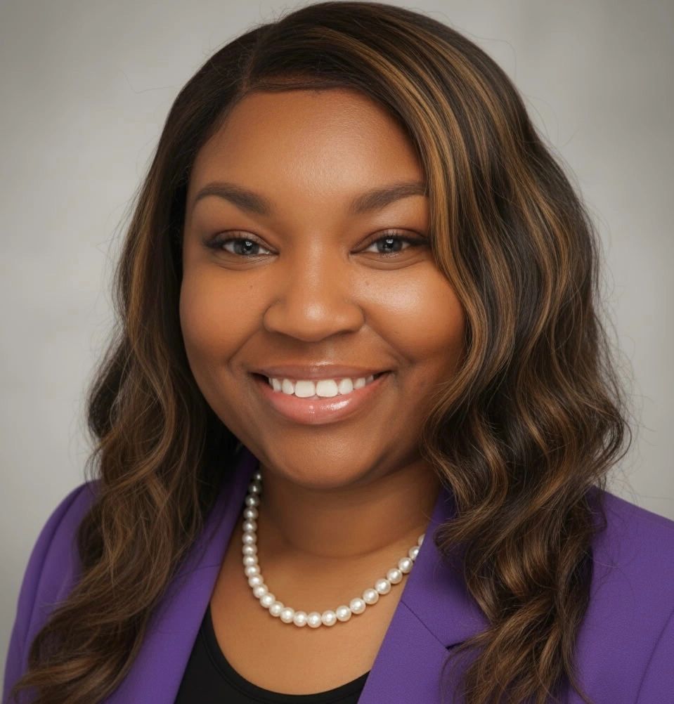 Smiling woman with wavy hair wearing a purple blazer and pearl necklace.