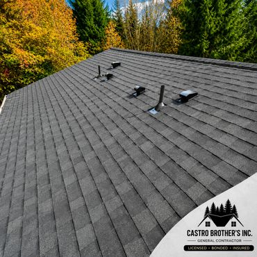 Newly installed asphalt shingle roof with vents and a backdrop of autumn trees.