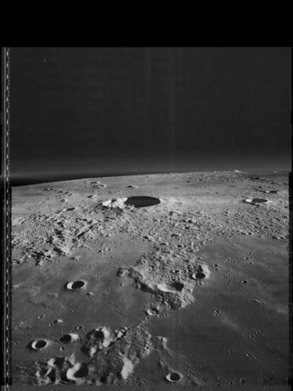 Black and white image of a cratered lunar surface under dark sky.
