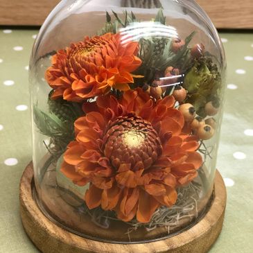 Orange flowers preserved under a glass dome with a wooden base.