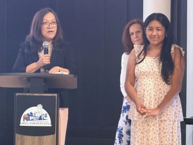 Woman speaking at a podium with two women standing beside her.