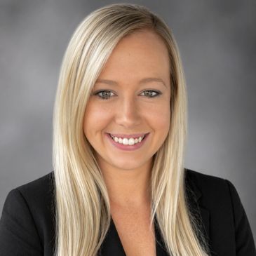 Professional portrait of a smiling woman with long blonde hair in business attire.