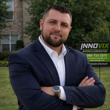 Confident man in a suit posing outdoors with a construction company sign behind him.