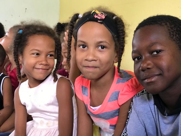Three children sitting closely together, smiling and enjoying each other's company.
