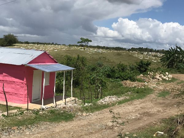 Pink house beside a dirt road under cloudy sky in a rural area.