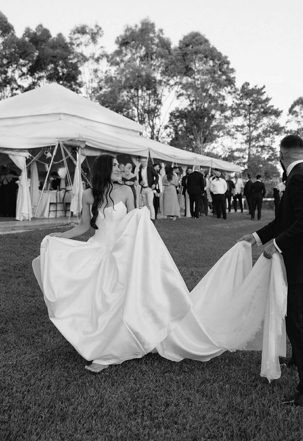 Bride and groom share a joyful moment outdoors, with the groom holding the bride's long train.