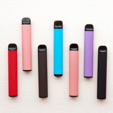 A group of different coloured disposable vapes on a plain background.