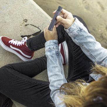 A young female sat on the pavement next to a road vaping.