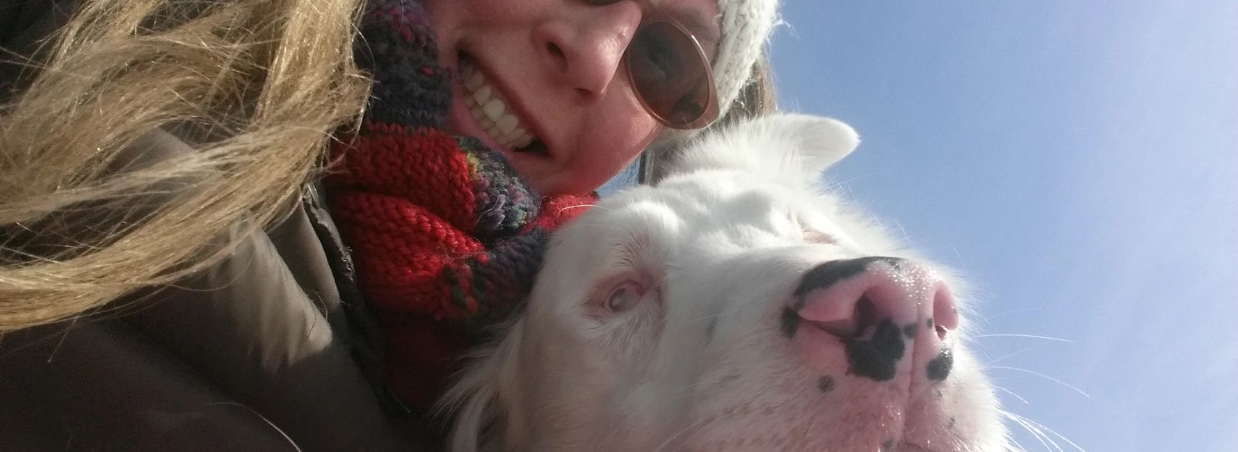 Woman with long hair wearing sunglasses with white dog