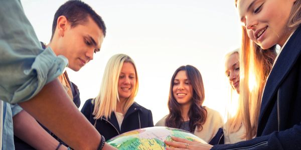 Jovens sorrindo e segurando um globo do mundo no centro da imagem.