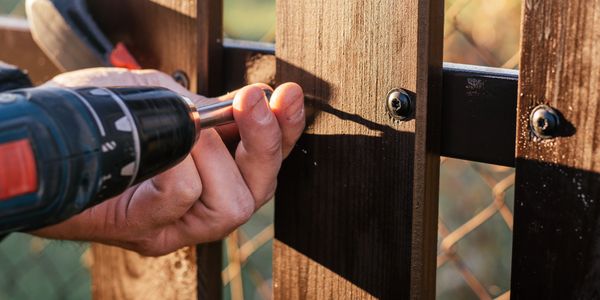 Hand of carpenter holding stud driving machine putting screw into wooden plank to metal construction