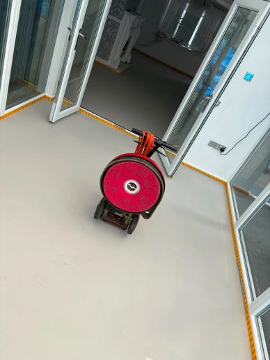 Red floor cleaning machine in an empty room with open glass doors.