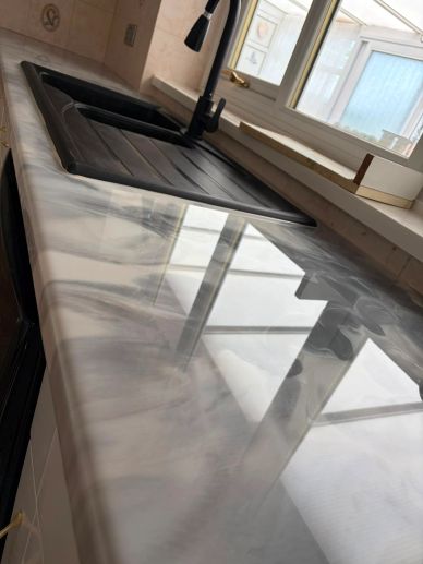 Glossy marble kitchen countertop with sink and window reflection.