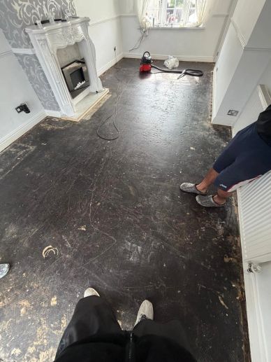Room under renovation with dark bare floor and two people.