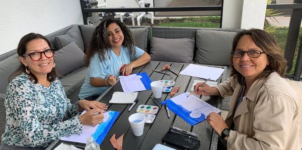 three women sitting at a table and painting 