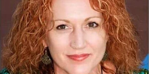 Portrait of a woman with curly red hair and a warm smile.