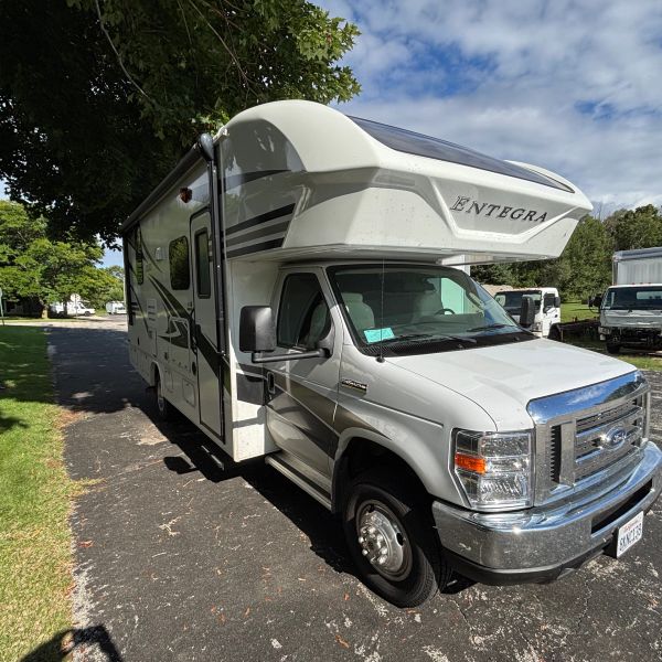 A white Entegra RV parked on a driveway under a partly cloudy sky.