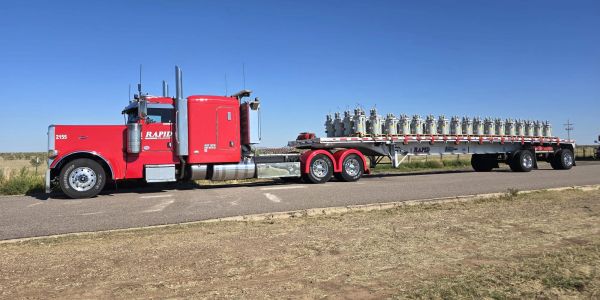 Red semi truck with a flatbed trailer carrying industrial equipment.