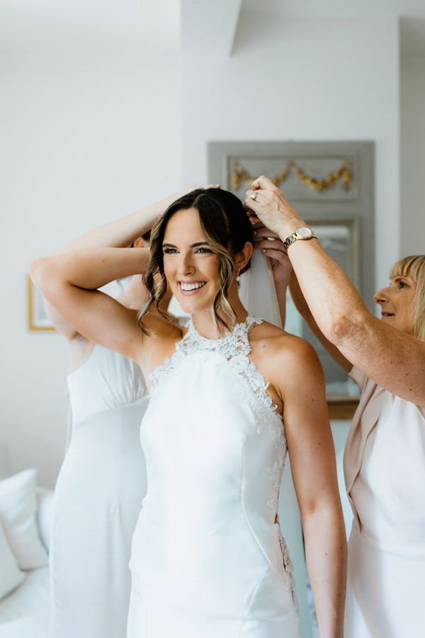 Bride smiling as she gets ready with help adjusting her veil.