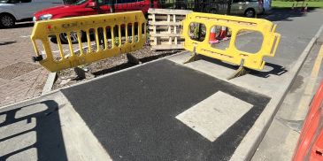 Temporary yellow barriers around a patched sidewalk section.