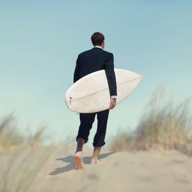 Une homme en costume, une planche de surf sous le bras