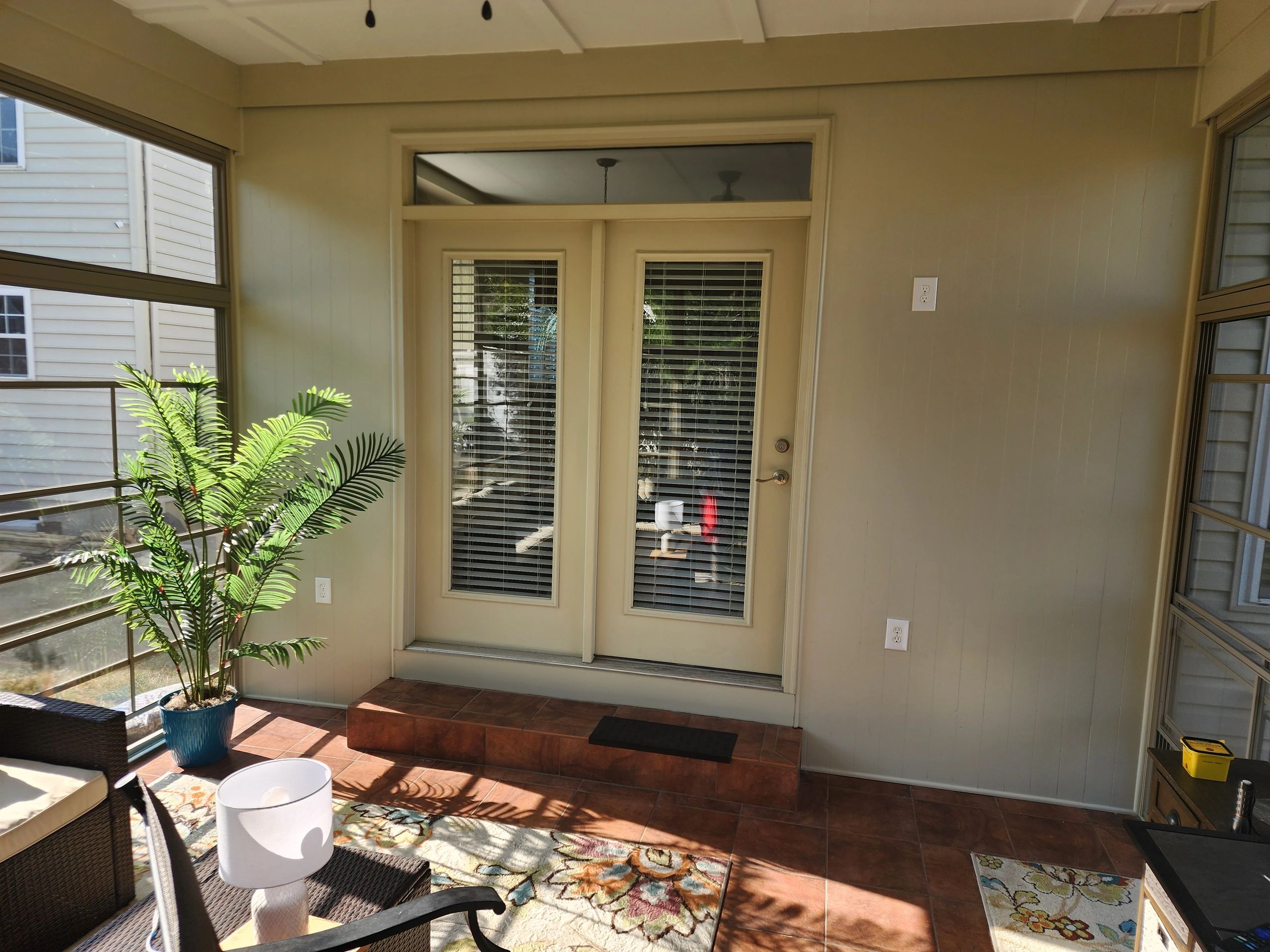 Sunlit patio with glass doors, a potted plant, and cozy seating area.
