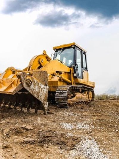 Yellow bulldozer with a ripper attachment on a construction site.