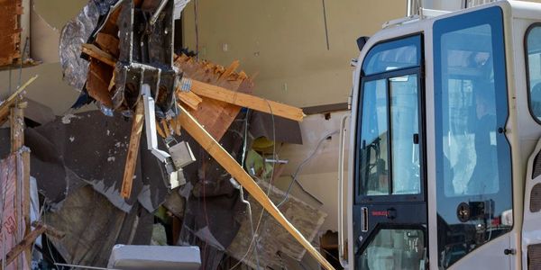 Excavator demolishing a building wall with debris falling.