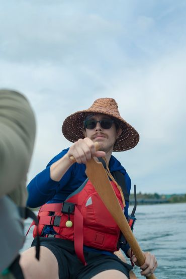 Man paddling a boat wearing a straw hat and life jacket.