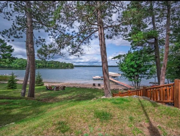 Lake view with trees, dock, and chairs.