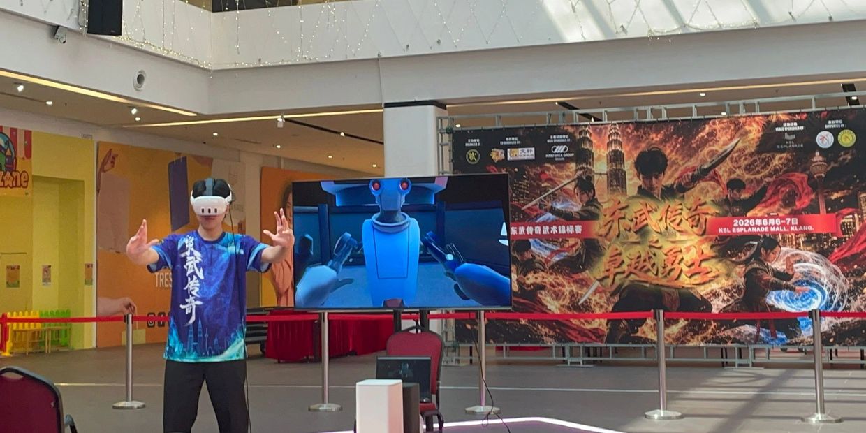 Person using VR headset in a modern indoor setting with a large screen and promotional banners.