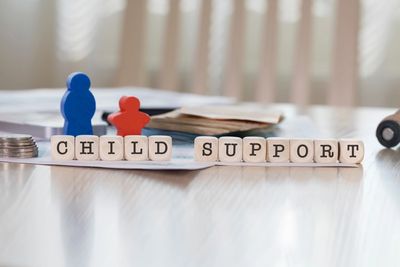 Wooden blocks spell out 'Child Support' with blue and red figurines on a table.