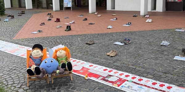 Viele Schuhe liegen auf dem Boden vor einem Gebäude.