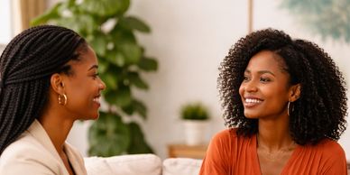 Two women smiling and chatting indoors, enjoying a friendly conversation.