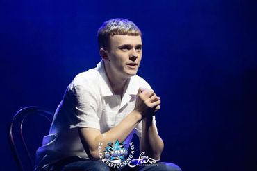 Young man performing on stage with intense focus under blue lighting.