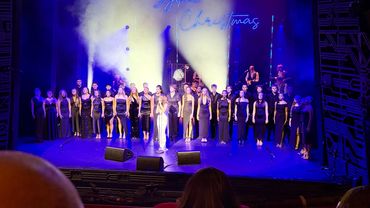 A large choir in formal attire performing on stage with Christmas lights.