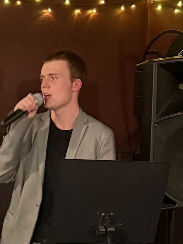 Young man singing into a microphone with a music stand.
