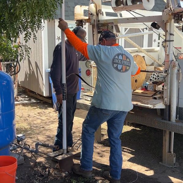Two workers operate equipment near a truck.