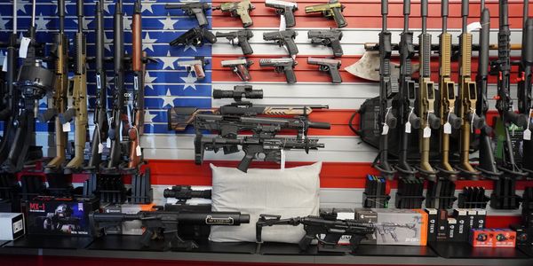 A wide array of firearms displayed against an American flag backdrop.