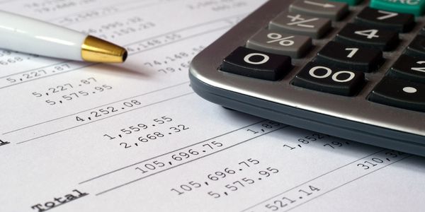 Calculator and pen on financial documents with totals and figures.
