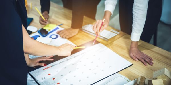 Team planning and discussing schedules over a calendar on a wooden table.