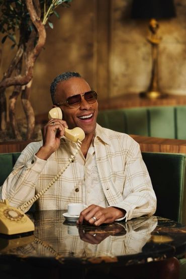 Man in sunglasses happily chatting on a vintage rotary phone.