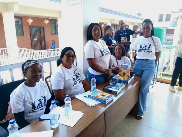 Group of people at a table with books and water bottles, wearing DRF Launch shirts.